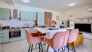A modern kitchen with teal cabinets, a central island, and pink chairs. - Luxurious home in Vodnjan (Vodnjan)
