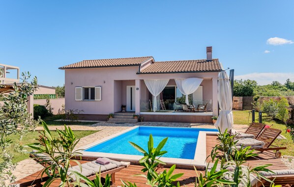 A two-story house with a swimming pool, outdoor seating, and a garden.