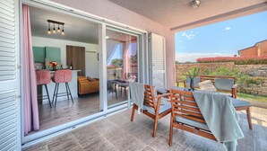 A spacious balcony with a wooden table and chairs, a sliding glass door leading to an interior dining area, and a view of a stone wall and garden. - Luxurious home in Vodnjan (Vodnjan)