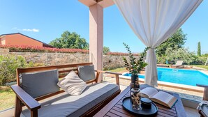 A covered outdoor seating area with a pool view, stone wall, and greenery. - Luxurious home in Vodnjan (Vodnjan)