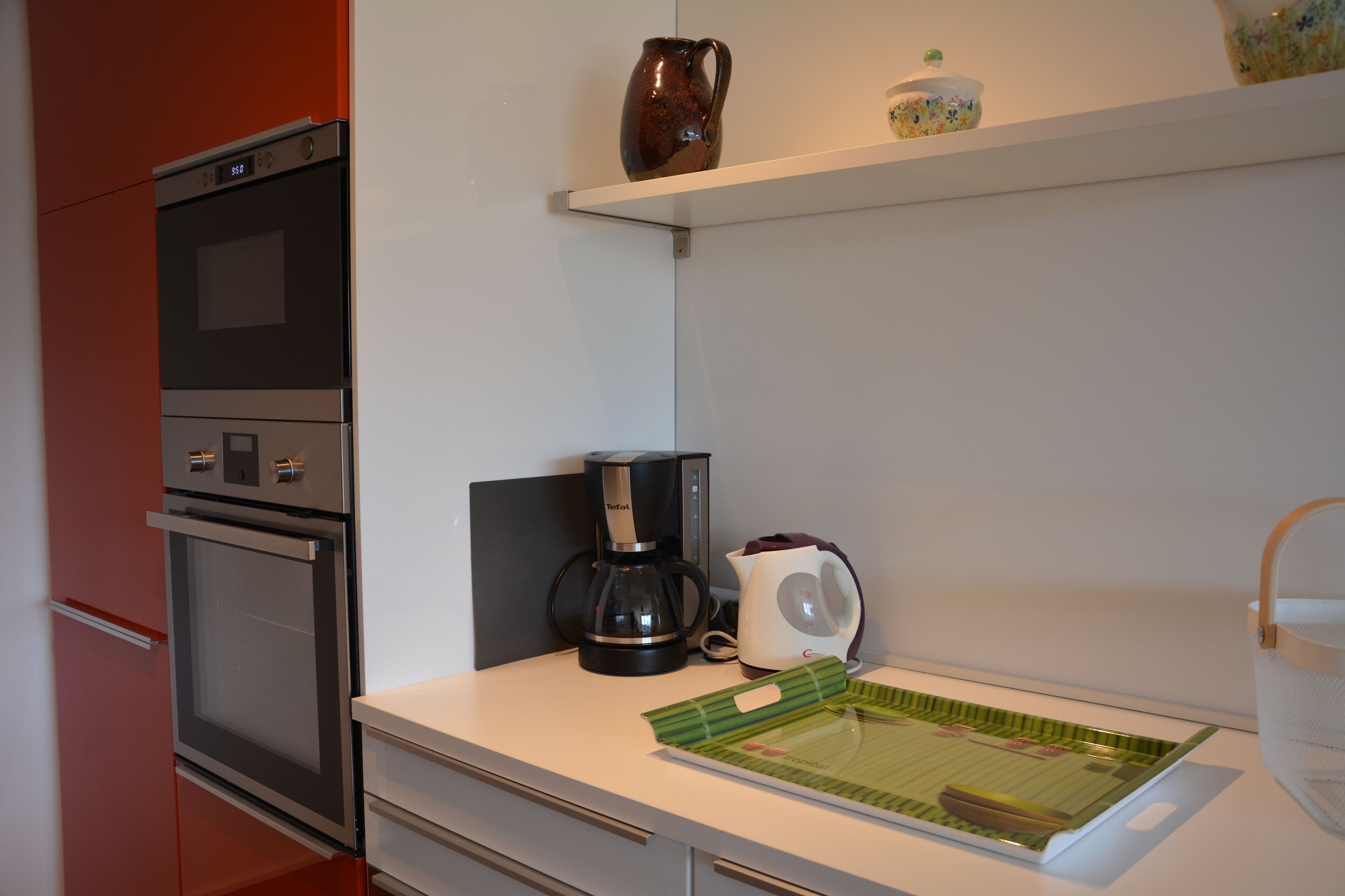 A kitchen with a coffee maker, kettle, and a green cutting board on the counter.