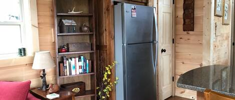 Interior acogedor de una cabaña con detalles de madera, una estantería empotrada, un refrigerador, una mesa de comedor y una silla roja.