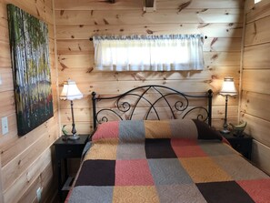 Een houten kamer met een bed, twee nachtkastjes, een lamp op elk, een schilderij aan de muur en een raam met gordijnen.