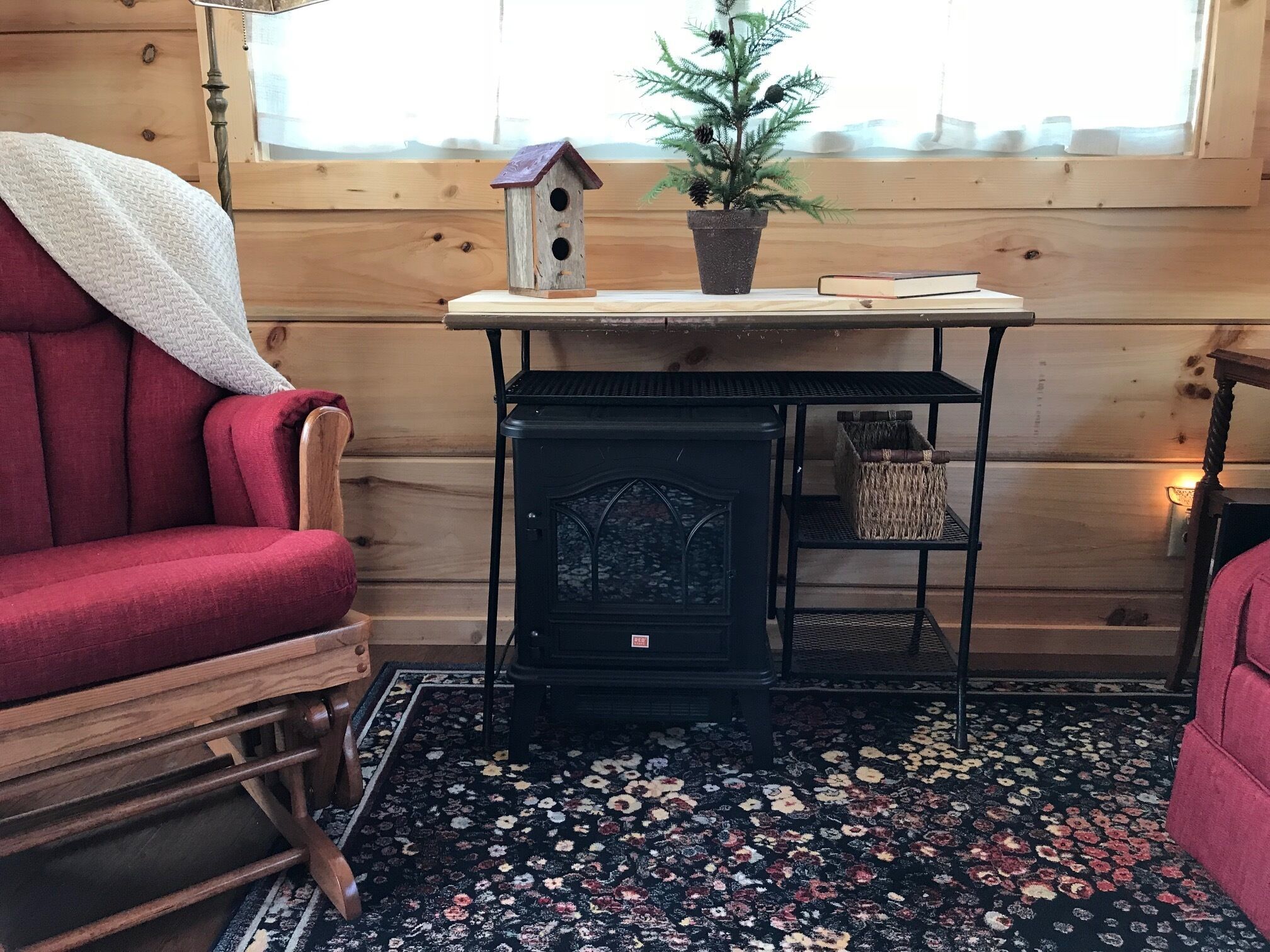 A cozy room with a red armchair, a small table with a potted plant, a decorative birdhouse, and a vintage stove.