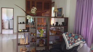 Un soggiorno con un divano in pelle nera, mensole in legno con diversi oggetti decorativi, una tenda viola e vista sulla cucina sullo sfondo.