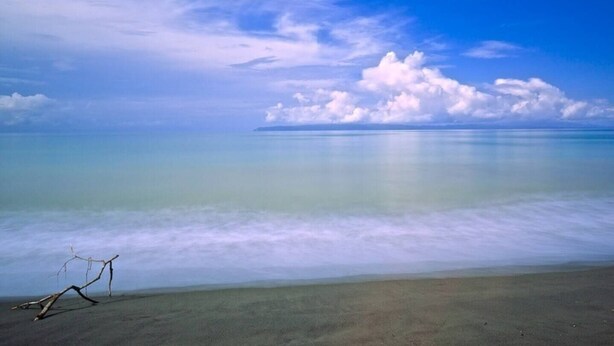 Ein Strand mit blauem Himmel, ruhiger See und einer fernen Insel.