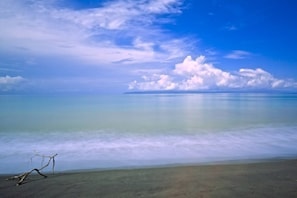 Une plage avec un ciel dégagé, une mer calme et une île qui se profile à l’horizon.