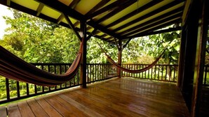 Eine Holzterrasse mit einer Hängematte und Geländer, umgeben von üppigem Grün.