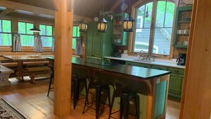 A rustic kitchen with a central island, wooden bar stools, and green cabinets.