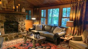 A cozy cabin interior with a stone fireplace, leather sofa, and a patterned rug.