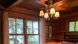 A wooden cabin bedroom with a bed, a nightstand, a chair, and a window with curtains.