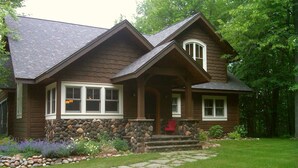 A two-story wooden house with a stone foundation, a stone pathway leading to the front door, and a well-maintained lawn.
