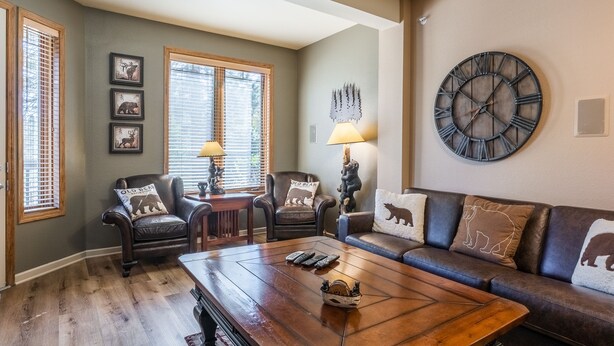 A living room with a wooden coffee table, leather sofas, and a large wall clock. - Mammoth Green #105 - Nearly Ski-in Ski-Out Updated 2 Bedroom 2 Bath, Sleeps 6 (Mammoth Lakes)