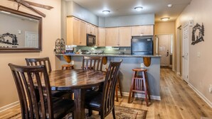 A kitchen with wooden cabinets, a central island, and a dining area with a wooden table and chairs. - Mammoth Green #105 - Nearly Ski-in Ski-Out Updated 2 Bedroom 2 Bath, Sleeps 6 (Mammoth Lakes)
