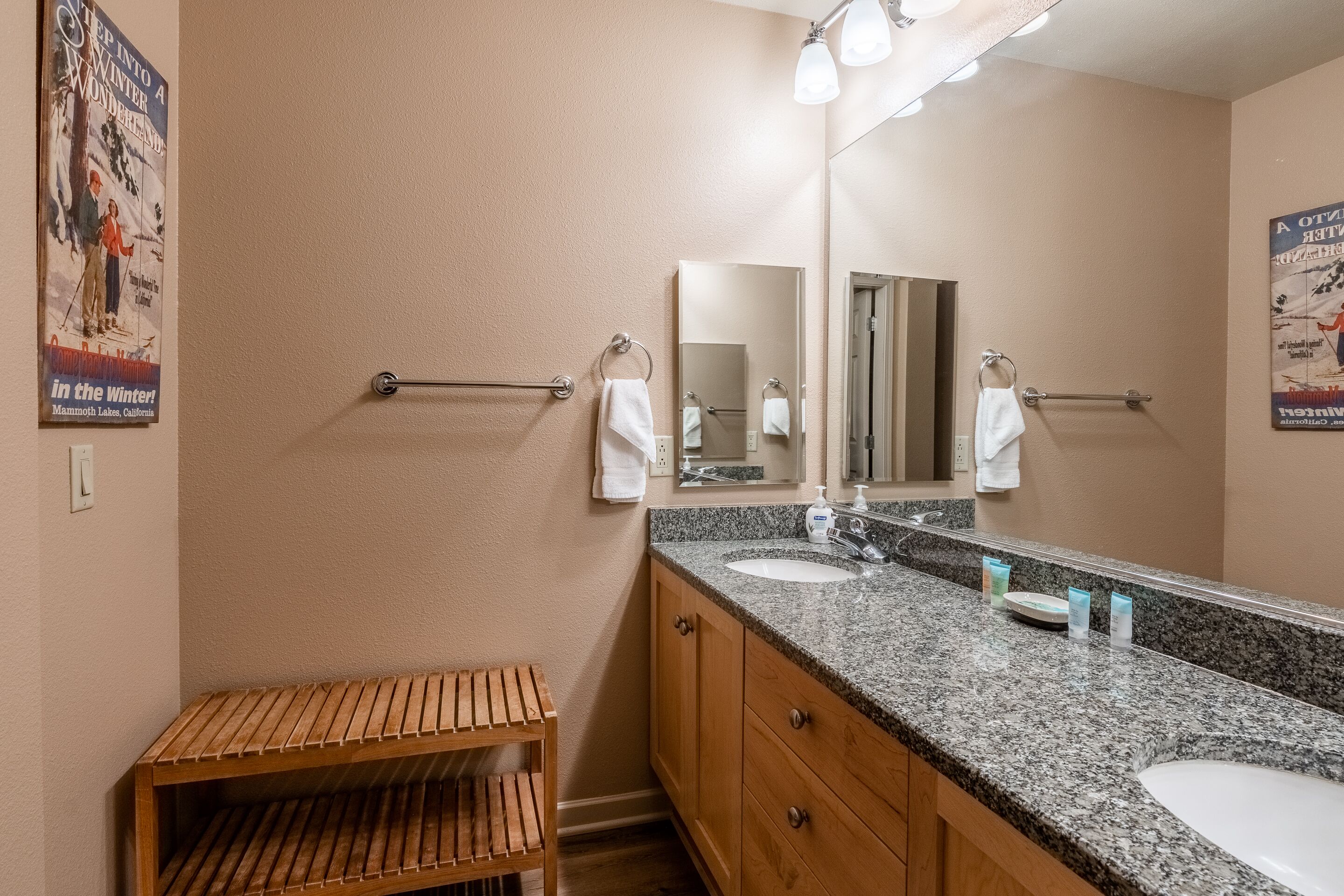 Une salle de bain avec un comptoir en granit, un lavabo, un miroir et un banc en bois.