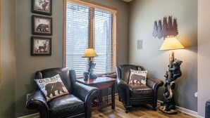 A room with two leather chairs, a wooden table, and a lamp. There are three framed pictures on the wall. - Mammoth Green #105 - Nearly Ski-in Ski-Out Updated 2 Bedroom 2 Bath, Sleeps 6 (Mammoth Lakes)