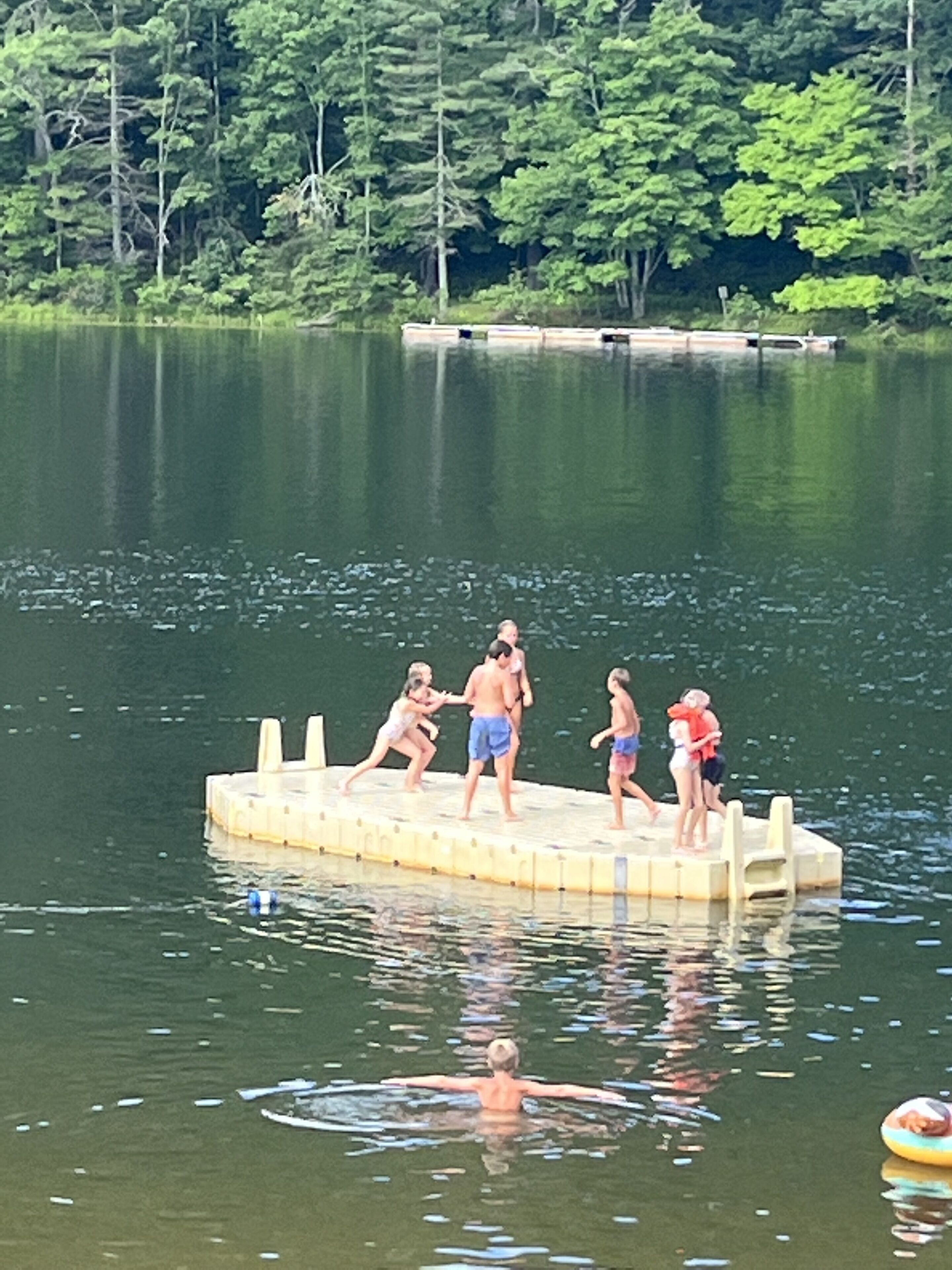 A group of people on a floating dock in a lake surrounded by trees.