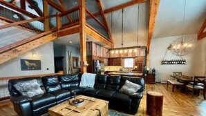 Un vaste espace de vie comprenant un grand canapé d’angle en cuir noir, une table basse en bois et un plancher en bois au style rustique.