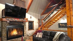 Un salon chaleureux avec une cheminée en pierre, un canapé en cuir noir et un escalier en bois.