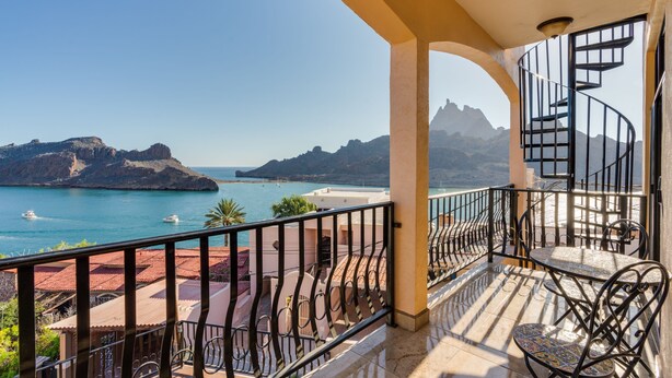 Un balcon avec vue sur la mer et les montagnes, un escalier en colimaçon et du mobilier d’extérieur.