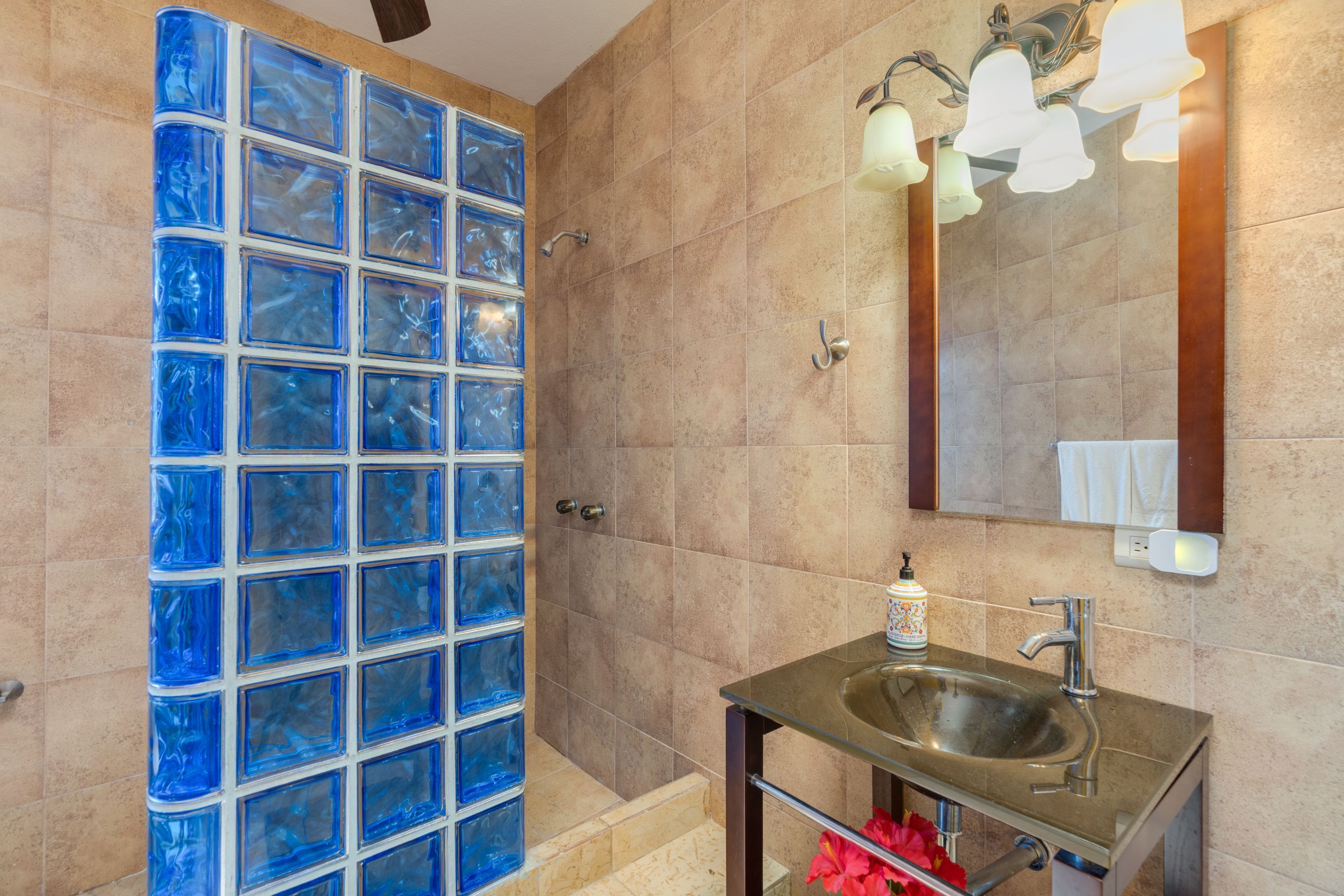A bathroom with a glass shower enclosure, a sink with a mirror, and a light fixture above the mirror.