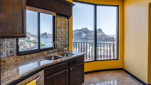 Une cuisine dotée de plans de travail en granit, de meubles en bois foncé et d’une grande fenêtre offrant une vue sur une côte rocheuse.
