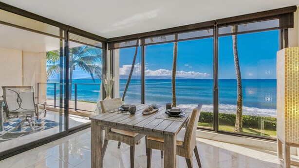 Ein geräumiger Balkon mit Blick auf den Ozean, ein Holztisch und Korbstühle.