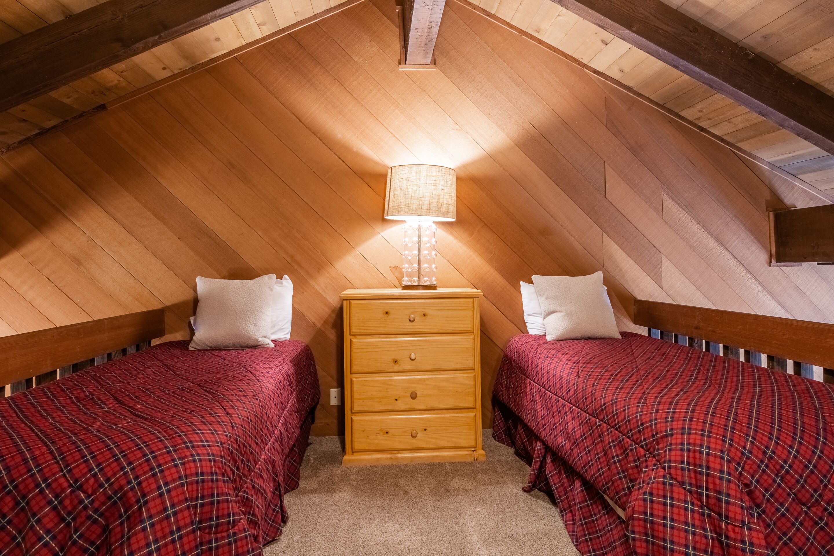 A small, cozy attic bedroom with two beds, a wooden dresser, and a lamp.