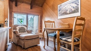 A cozy room with wooden walls and a large window. There is a chair with a cushion, a small table, and a framed picture of a mountain. - Snowcreek #97 - Great Views. Large. 2 bedroom + loft, 2 bathroom, 3-level condo. Sleeps 8 (Mammoth Lakes)