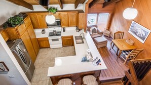 A modern kitchen with wooden cabinets, a central island, and a dining area with wooden furniture. - Snowcreek #97 - Great Views. Large. 2 bedroom + loft, 2 bathroom, 3-level condo. Sleeps 8 (Mammoth Lakes)