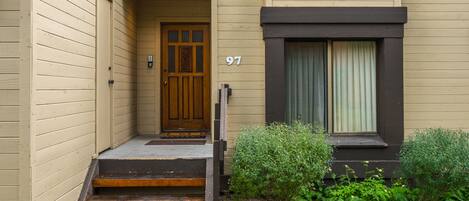 Un bâtiment de couleur beige, avec une porte en bois, le numéro 97, et une fenêtre avec des rideaux.