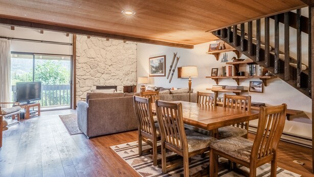 A spacious living area with a wooden dining table, comfortable seating, a stone accent wall, and a staircase leading to an upper level. - Snowcreek #97 - Great Views. Large. 2 bedroom + loft, 2 bathroom, 3-level condo. Sleeps 8 (Mammoth Lakes)