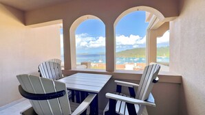 Ein Balkon mit Tisch und zwei Stühlen, Blick auf einen Yachthafen mit Booten und eine hügelige Landschaft.