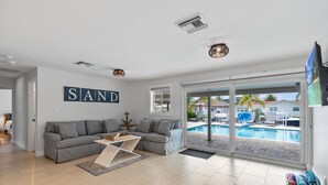 En moderne stue med en grå sofa, et træbord og et stort vindue med udsigt til en pool.