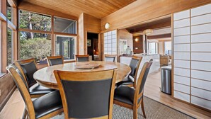 A wooden dining area with a round table and chairs, large windows, and a view of the outdoors. - Newly Renovated Oceanfront Retreat in Bolinas with Spa and huge fenced yard  (Bolinas)