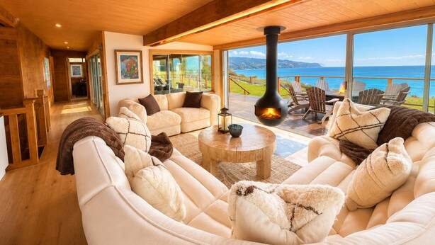 A cozy living room with a fireplace, large windows, and a view of the ocean. - Newly Renovated Oceanfront Retreat in Bolinas with Spa and huge fenced yard  (Bolinas)