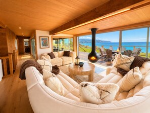 Un salon chaleureux avec une cheminée, de grandes fenêtres et une vue sur l’océan.