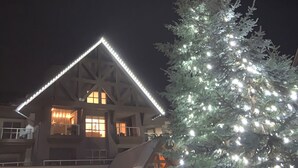 A building with a triangular roof and multiple windows, surrounded by a snow-covered tree with lights. - XL Luxury Penthouse. Top 1%. The Aspens. A/C, Pool, 3 hot tubs, ski-in ski-out.  (Whistler)