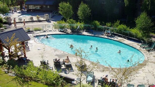 A pool area with lounge chairs and a building in the background. - XL Luxury Penthouse. Top 1%. The Aspens. A/C, Pool, 3 hot tubs, ski-in ski-out.  (Whistler)
