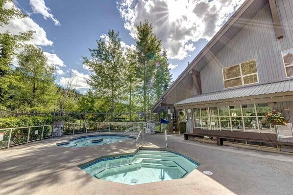 A pool area with a wooden deck, a covered seating area, and a building with large windows.