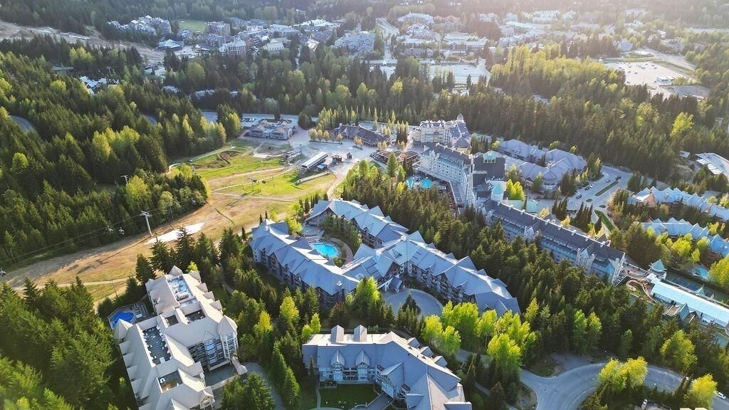 An aerial view of a resort with multiple buildings, including a large hotel with a pool and a smaller building with a dome structure.
