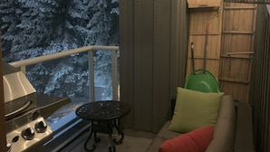 A cozy outdoor seating area with a grill, a view of snow-covered trees, and a wooden deck. - XL Luxury Penthouse. Top 1%. The Aspens. A/C, Pool, 3 hot tubs, ski-in ski-out.  (Whistler)