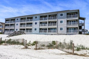 Un grand hôtel en bord de mer, avec plusieurs étages et des balcons, une plage de sable en premier plan et un ciel dégagé.