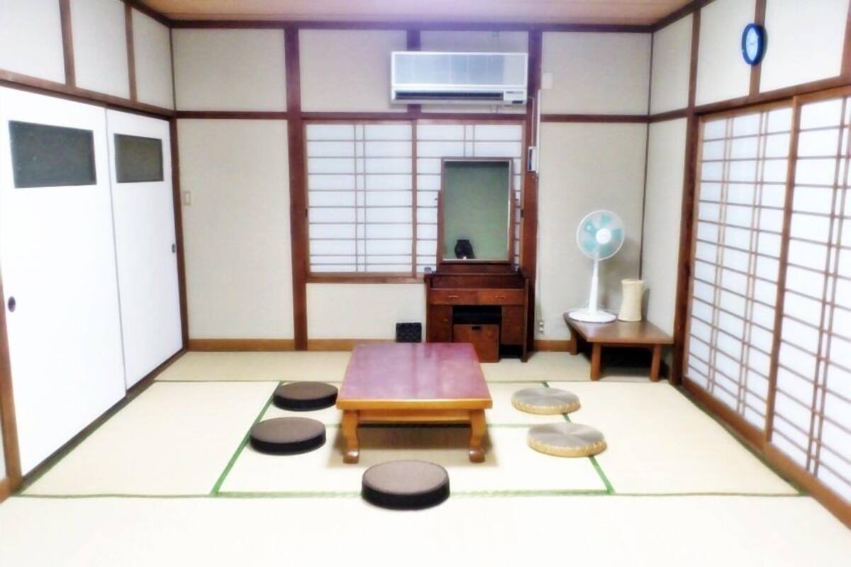 Une pièce de style japonais traditionnel, avec un sol recouvert de tatamis, un bureau en bois, un miroir, un éventail et des portes coulissantes.