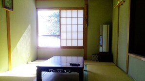 Une pièce avec un sol recouvert de tatamis, une petite table basse, un paravent coulissant de style shoji et un miroir de style japonais traditionnel.