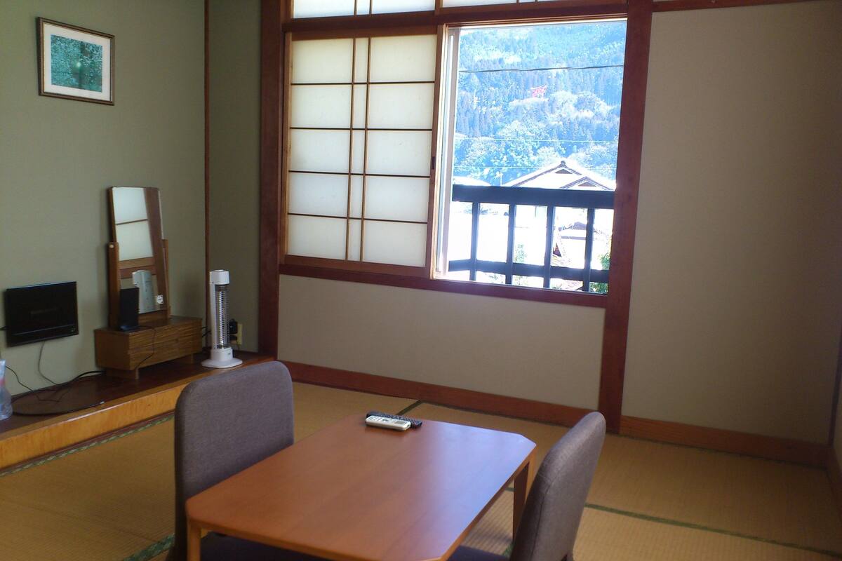Une pièce de style japonais traditionnel, avec un sol recouvert de tatamis, une petite table en bois et une grande fenêtre à panneaux coulissants de type shoji.