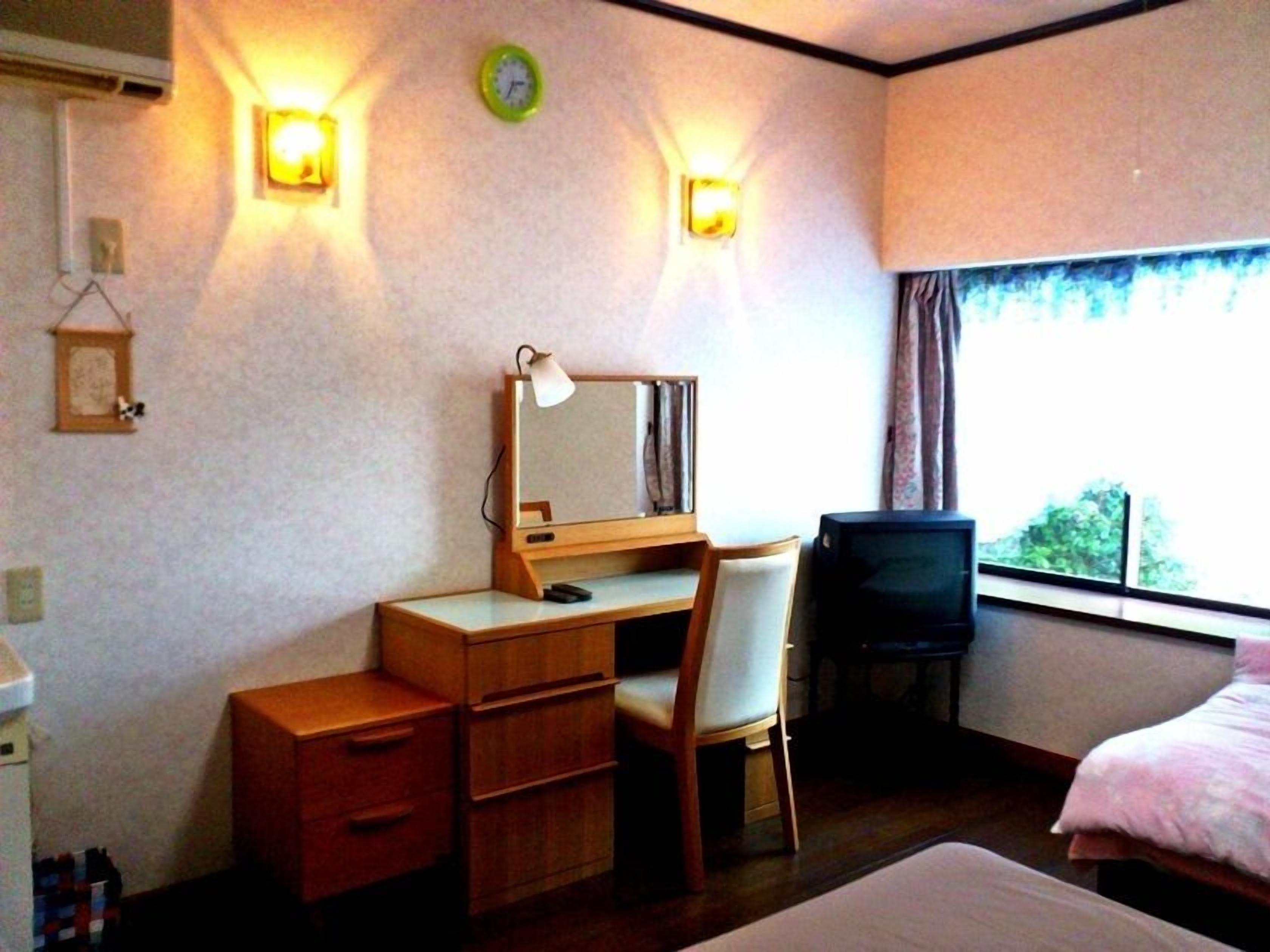 Een hotelkamer met een bed, een bureau met stoel, een televisie en twee wandlampen.