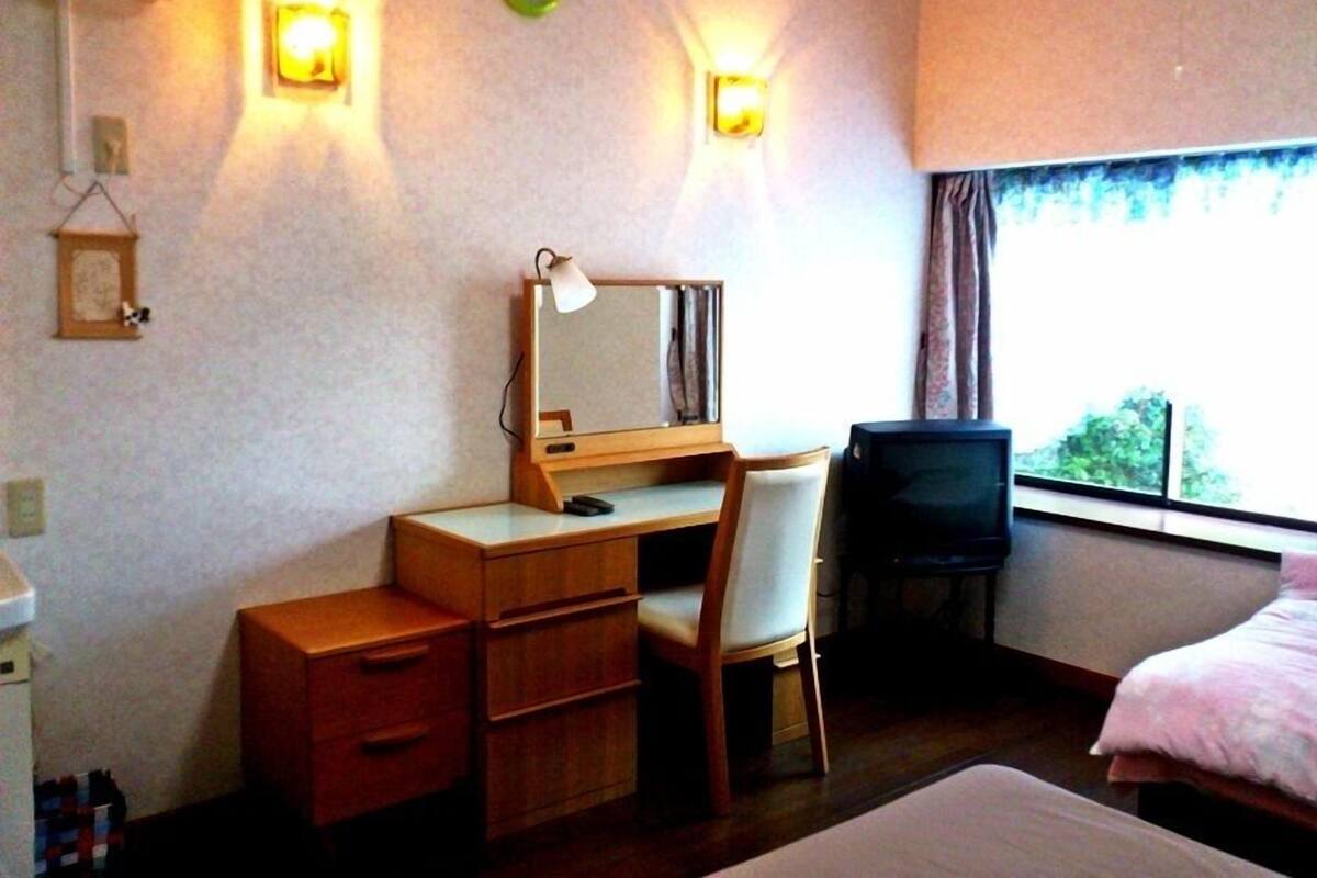 Une chambre d’hôtel comprenant un lit, un bureau avec une chaise, une télévision et deux lampes fixées au mur.