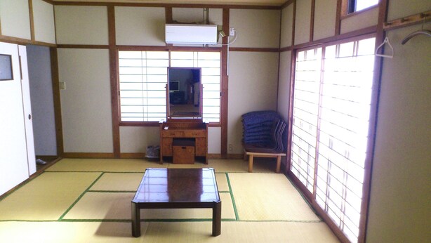 Une pièce de style japonais traditionnel, avec un sol recouvert de tatamis, une basse table en bois, une chaise, un petit meuble et une fenêtre dotée de panneaux coulissants en papier.