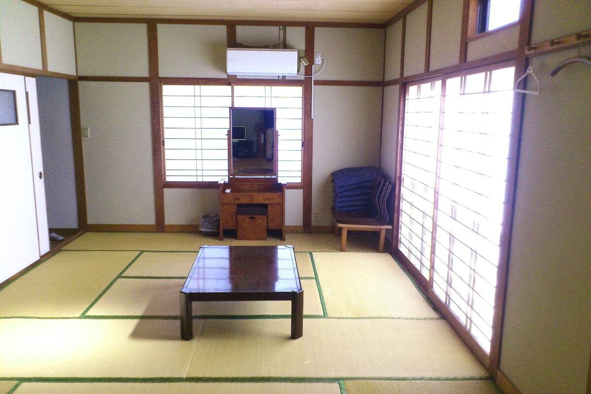 Une pièce de style japonais traditionnel, avec un sol recouvert de tatamis, une basse table en bois, une chaise, un petit meuble et une fenêtre dotée de panneaux coulissants en papier.